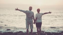 senior aged people open arms with ocean and sunset in front of them