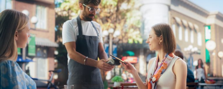 Allianz - woman paying server at cafe while traveling abroad
