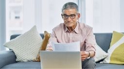 senior man reviewing paperwork in front of laptop